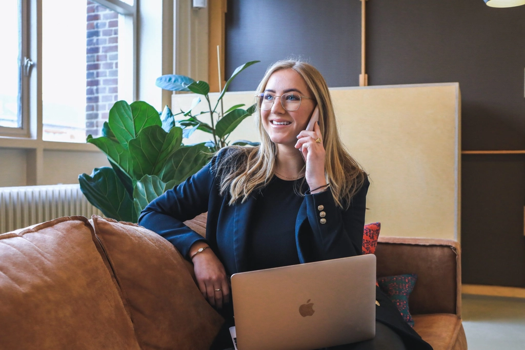 Businesswoman sitting on a couch with a laptop on her lap, talking on the phone.