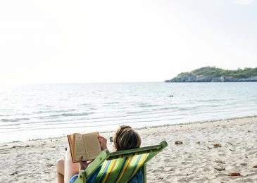 A woman relaxes in a deck chair by the sea.