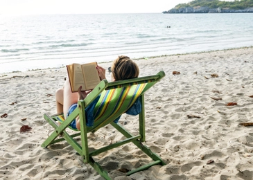 A woman relaxes in a deck chair by the sea.