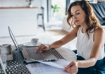 Woman using laptop while sitting at table. Young businesswoman sitting in kitchen and working on laptop.