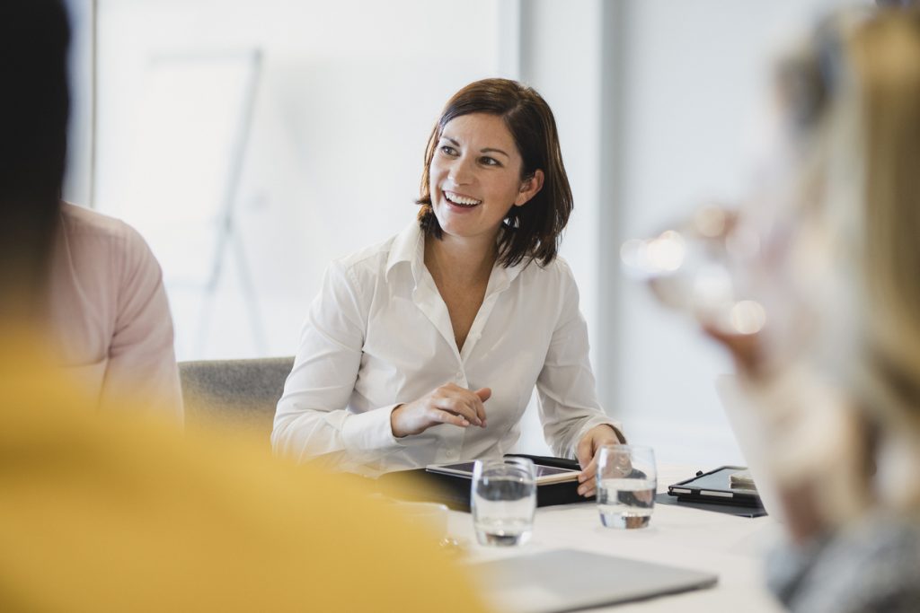 Businesswoman smiling at meeting table, listening, learning, success, happiness