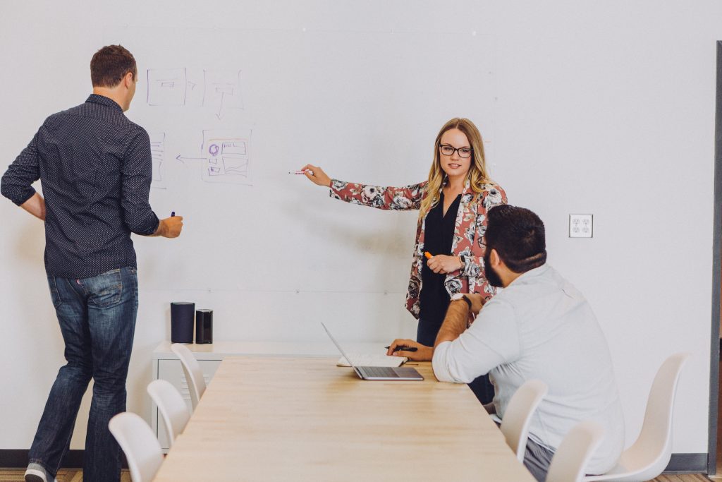 Effective leadership: people around the table listening to a woman who is presenting, explaining something. 